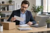 Un professionnel consulte une enveloppe et du courrier à côté d’un colis neutre dans son bureau.